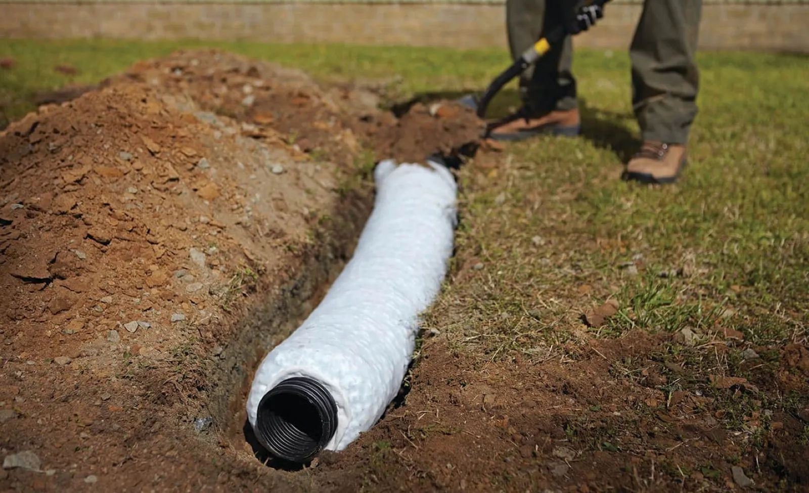 Perforated drain pipe wrapped in fabric laid in a gravel trench during a French drain install