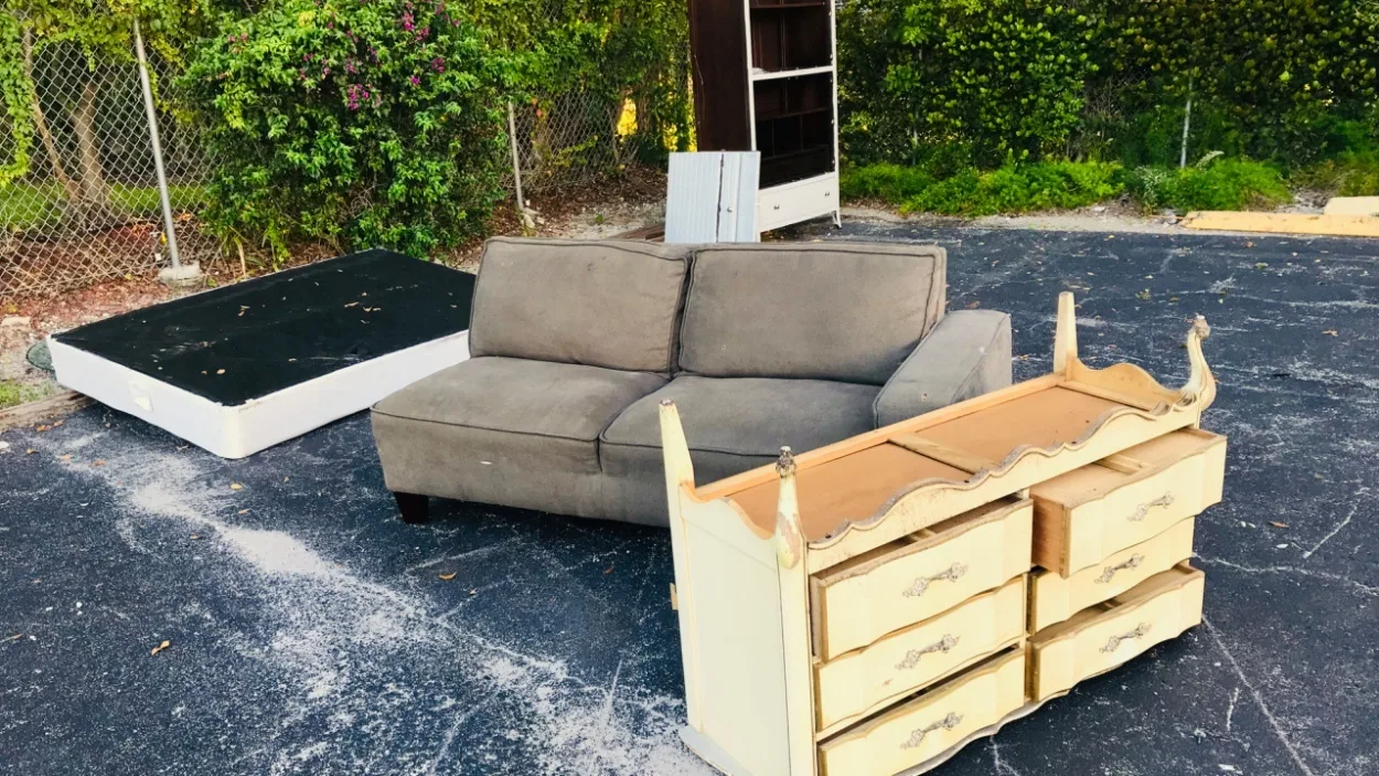 Old couch, box spring and dresser set out on a paved lot for junk removal