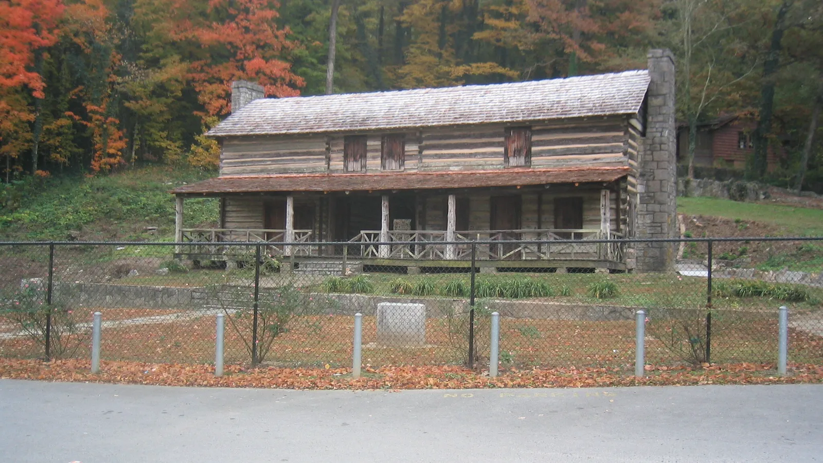 The historic John Ross House log cabin in Rossville, GA, with fall color on the wooded hillside behind it